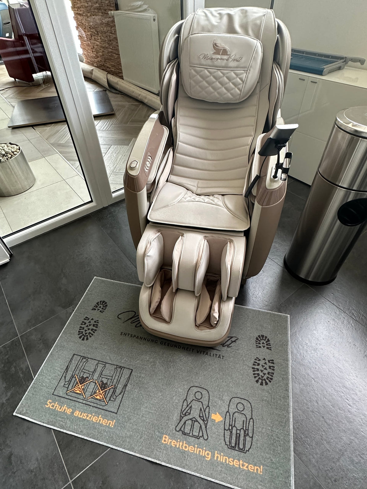 
Hinweis-Fußteppich „Schuhe ausziehen“ vor einem Massagesessel