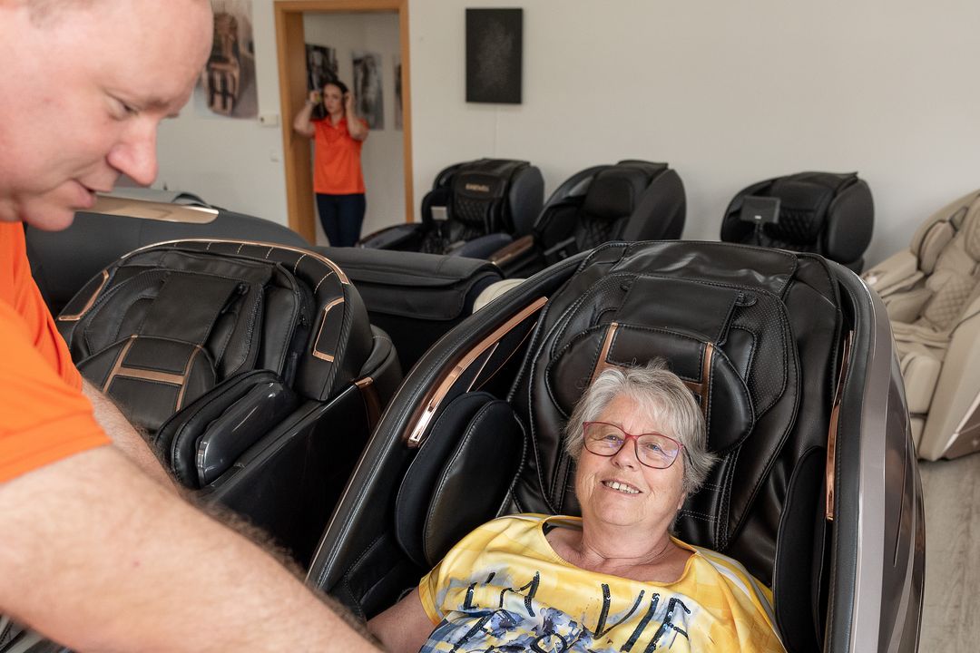 Ein Berater der Massagesessel Welt beugt sich zu einer Kundin, die im Massagesessel sitzt, und erklärt ihr die Bedienung